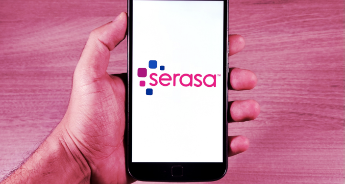 Mão segurando celular com aplicativo Serasa aberto na tela.