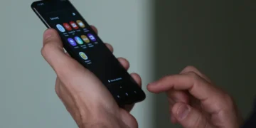 Imagem de uma mão segurando o celular, com vários aplicativos na tela.