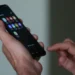 Imagem de uma mão segurando o celular, com vários aplicativos na tela.