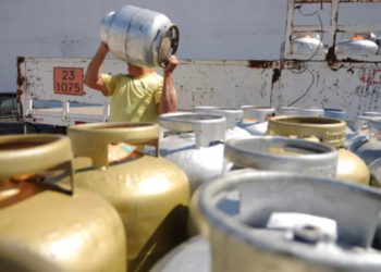 Homem carregando botijão de gás com outros botijões em segundo plano, ilustrando o contexto do benefício do 'Gás para Todos