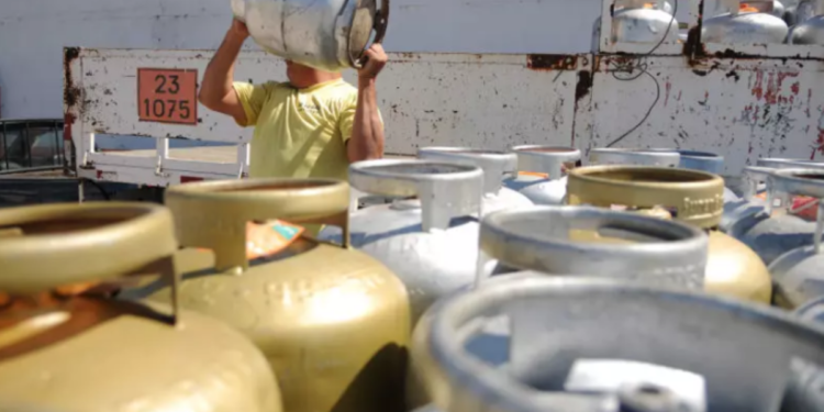 Homem carregando botijão de gás com outros botijões em segundo plano, ilustrando o contexto do benefício do 'Gás para Todos