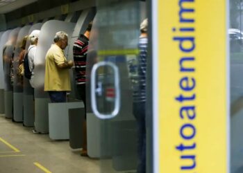 Imagem de pessoas utilizando caixas eletrônicos no banco, ilustrando o funcionamento das agências bancárias durante o carnaval.