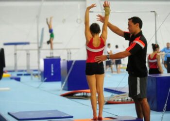 Treinamento de ginástica olímpica com apoio de um treinador, ilustrando a importância de bolsas de incentivo como o Bolsa Talento Esportivo.