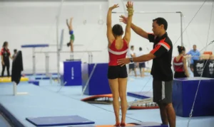 Atleta de ginástica sendo treinada com o auxílio de um técnico, representando a dedicação e esforço necessários para o Programa Bolsa Atleta.