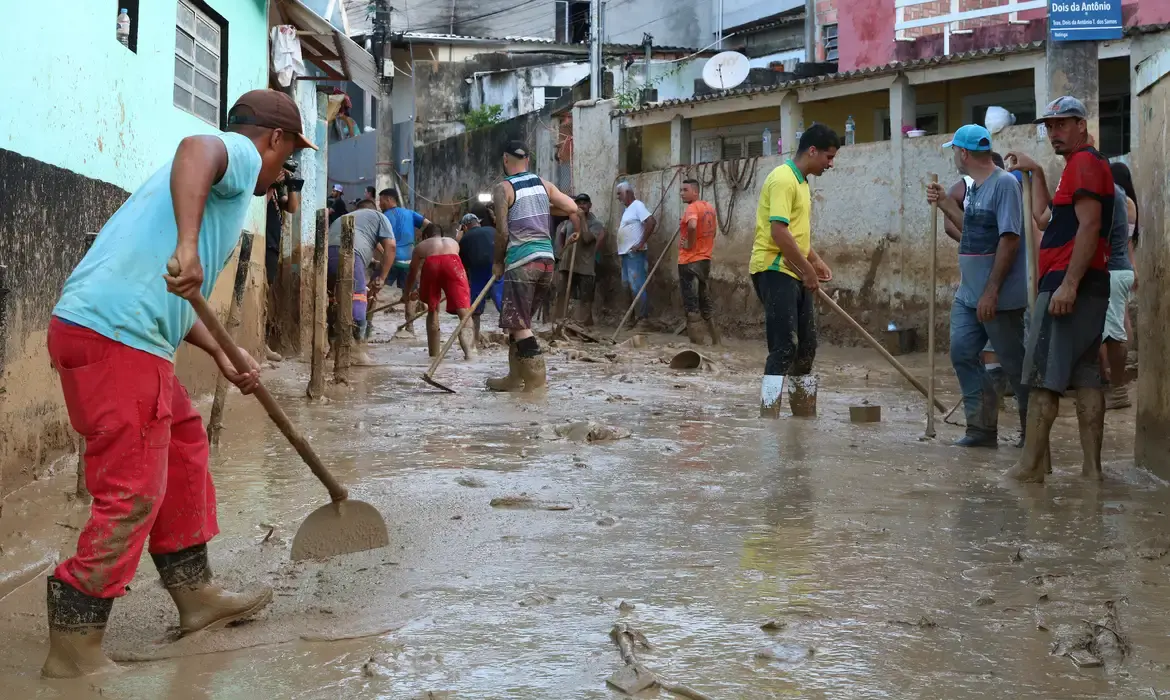 Grupo de pessoas trabalhando na limpeza de uma área alagada após desastre, relacionado ao Auxílio Reconstrução.