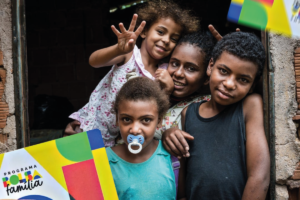 Imagem de crianças e uma mulher com o cartão do Bolsa Família nas mãos, representando famílias que se beneficiam dos adicionais do programa.