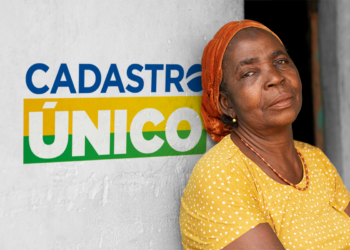 Mulher olhando para a câmera com fundo de parede com o logo do Cadastro Único (CadÚnico), destacando a importância do sistema.
