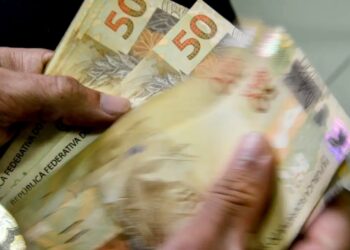 Notas de cinquenta reais sendo contadas, representando o pagamento do abono salarial PIS/PASEP.