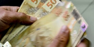 Notas de cinquenta reais sendo contadas, representando o pagamento do abono salarial PIS/PASEP.