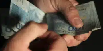 Notas de 100 reais sendo contadas, representando auxílio financeiro.