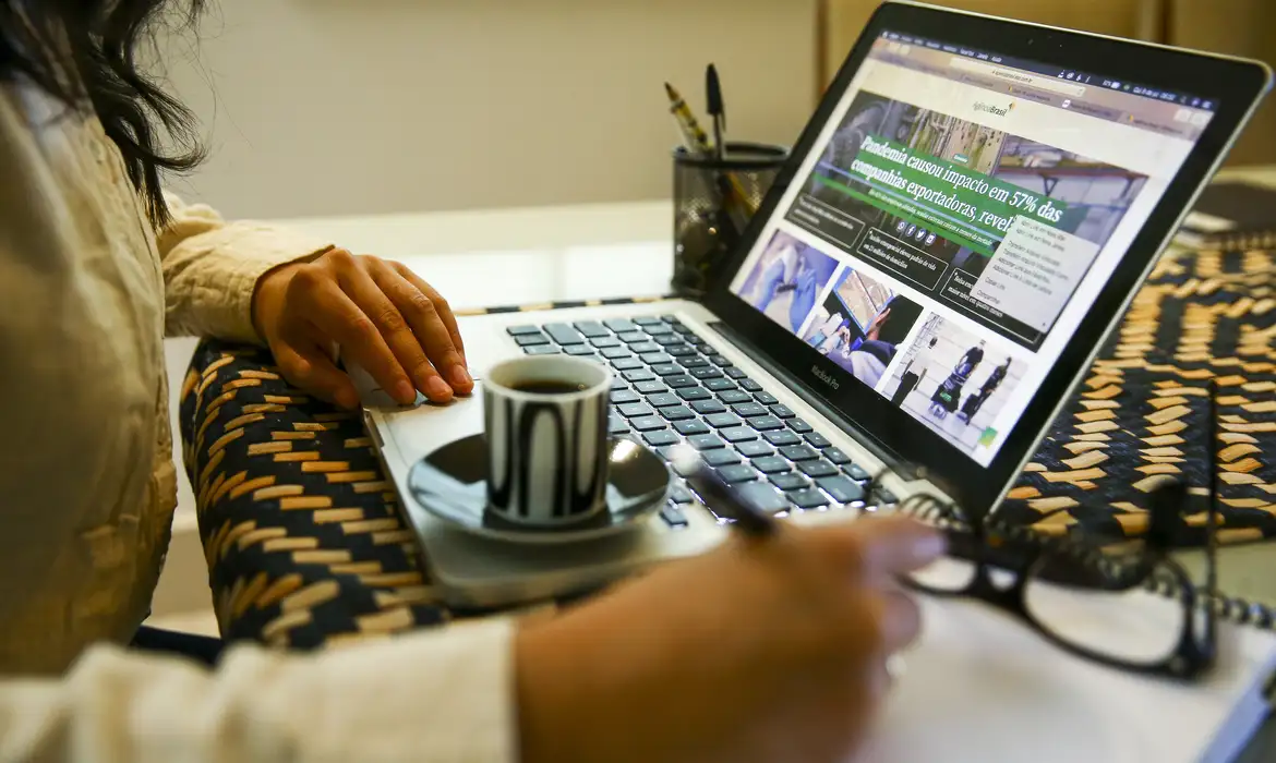 Pessoa acessando um site em um laptop com uma xícara de café ao lado.