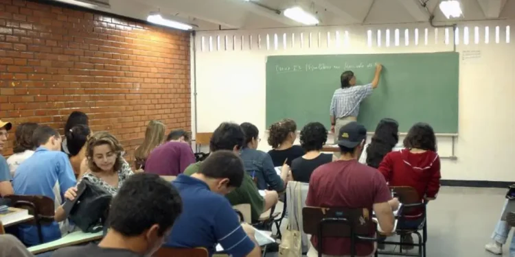 Estudantes em sala de aula assistindo a uma aula, com professor escrevendo no quadro negro.