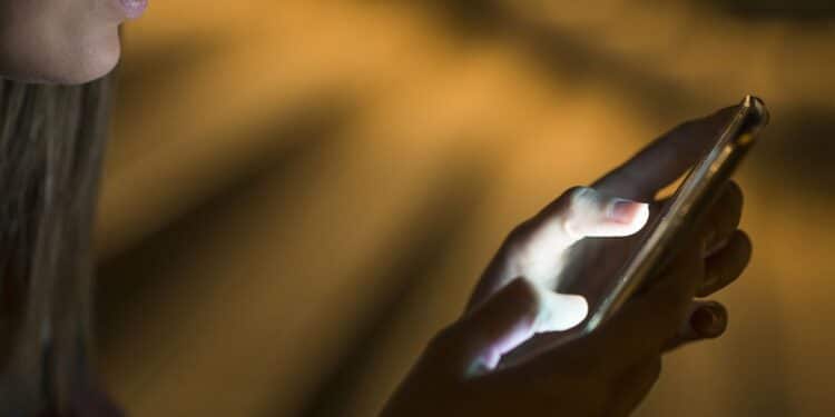 Pessoa usando o celular à noite, com luz de tela iluminando a tela, simbolizando a atenção necessária para evitar golpes.