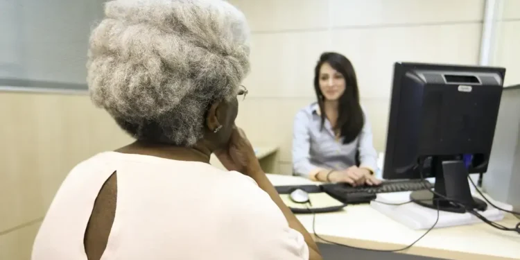 Mulher idosa sendo atendida por uma funcionária em um escritório governamental.