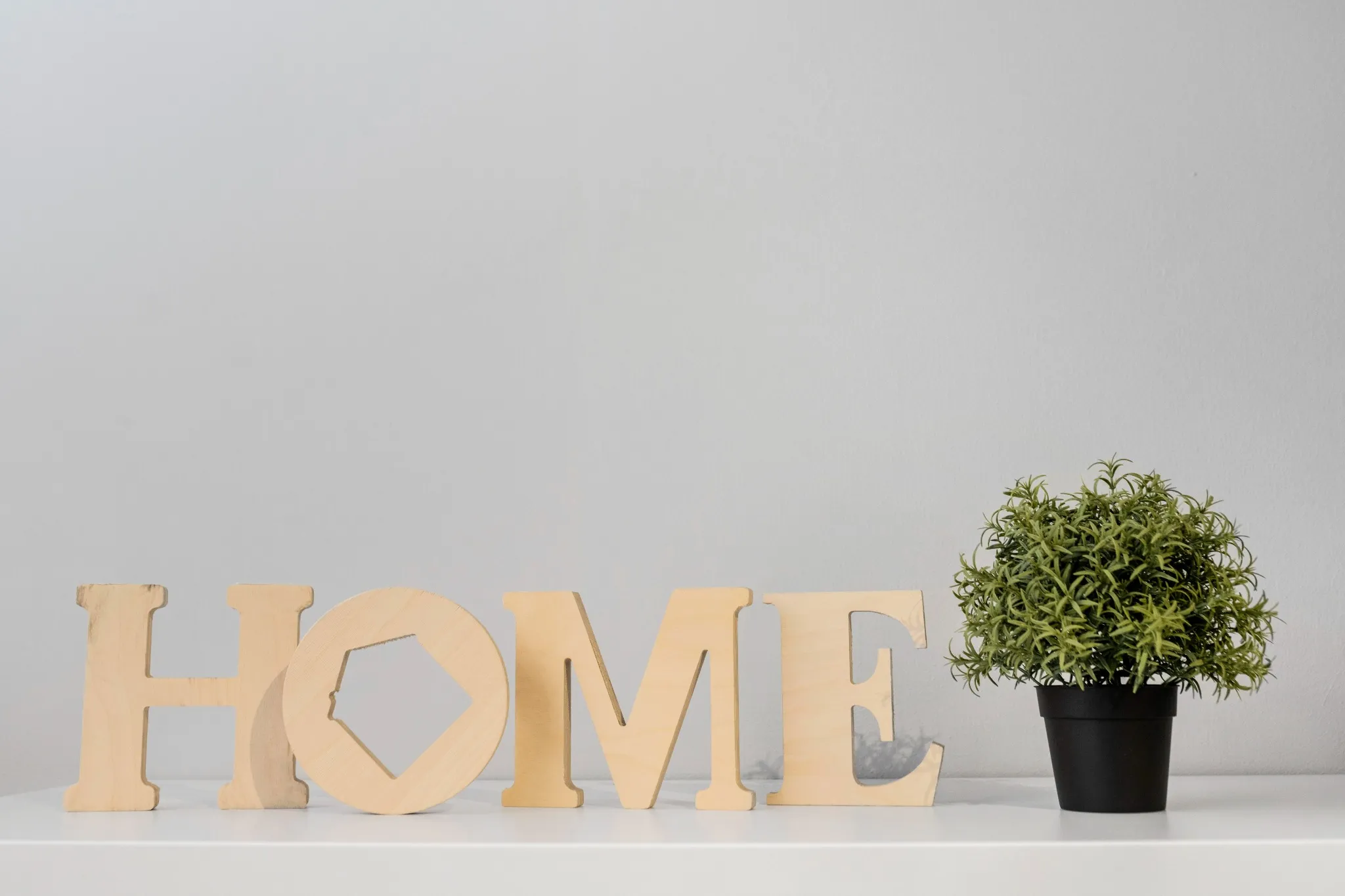 Decoração com letras de madeira formando a palavra "HOME" ao lado de um vaso de planta, representando um ambiente acolhedor.