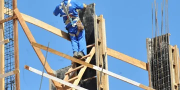 Trabalhador de construção civil subindo em uma estrutura de madeira, simbolizando esforços de reconstrução após um desastre.