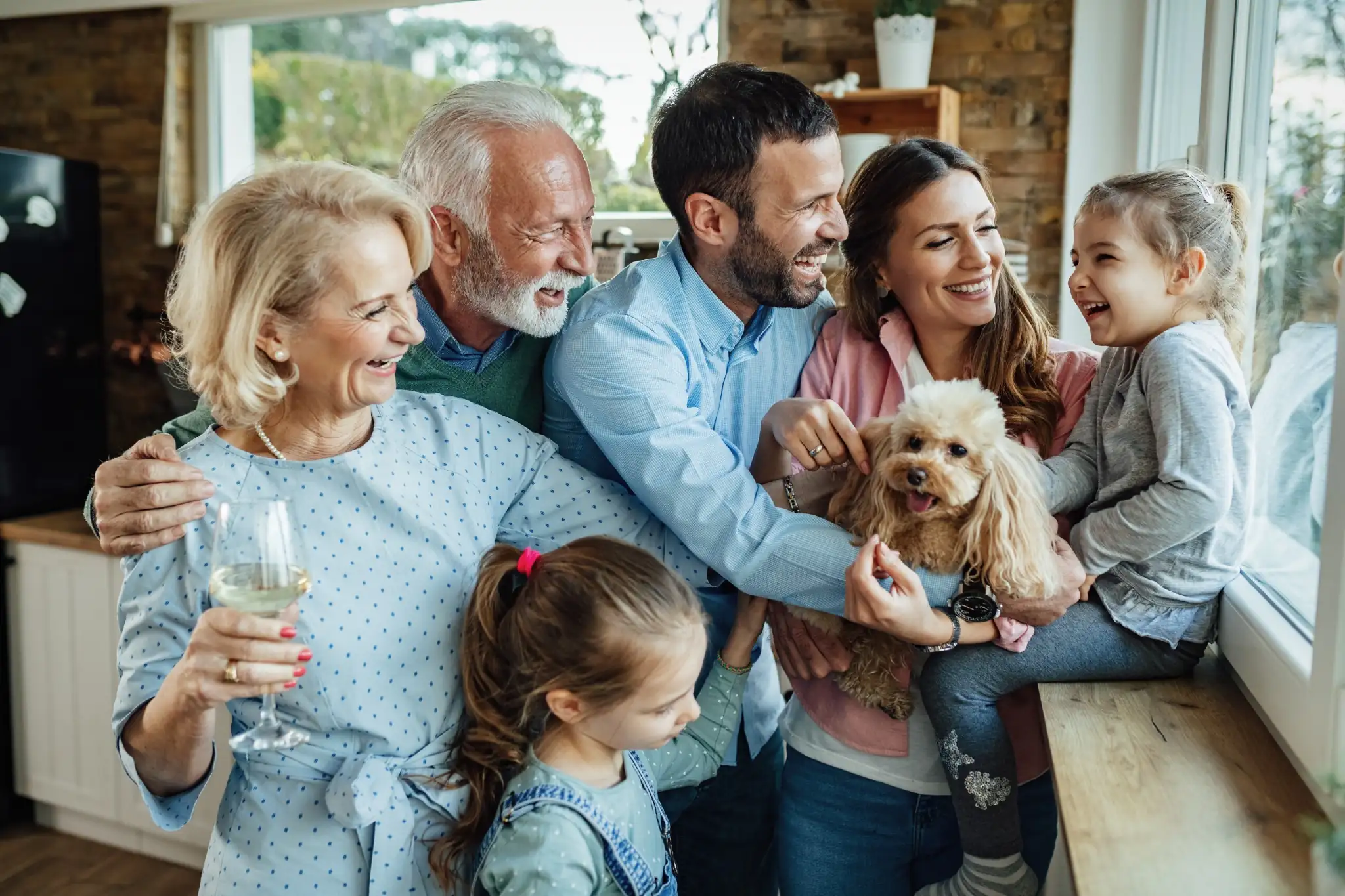 Família reunida em casa, sorrindo e interagindo com um cachorro de estimação.