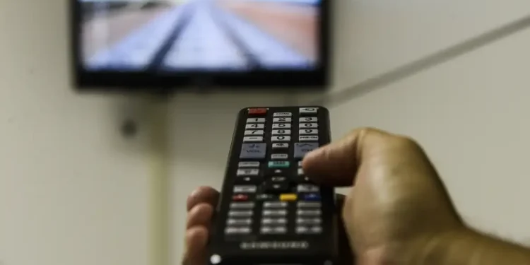 Pessoa controlando a TV com um controle remoto enquanto assiste à programação.