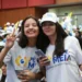 Duas estudantes sorridentes fazem pose em evento do programa Pé-de-Meia, rodeadas por outros participantes.