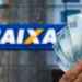 Notas de R$ 100 sendo exibidas em frente ao logotipo da Caixa Econômica Federal, simbolizando a liberação de recursos.