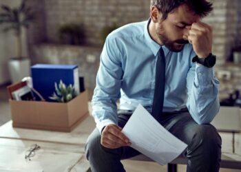 Homem frustrado sentado após ser demitido, refletindo sobre a situação de desemprego.