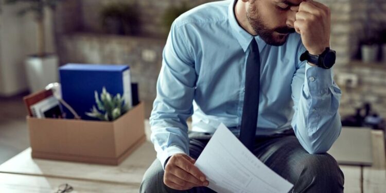 Homem frustrado sentado após ser demitido, refletindo sobre a situação de desemprego.
