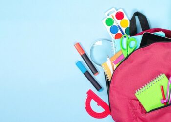 Mochila vermelha aberta com material escolar sobre fundo azul claro.