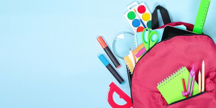 Mochila vermelha aberta com material escolar sobre fundo azul claro.