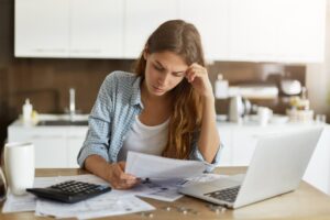 Mulher preocupada analisando contas e boletos, representando a necessidade do auxílio para quitar dívidas.