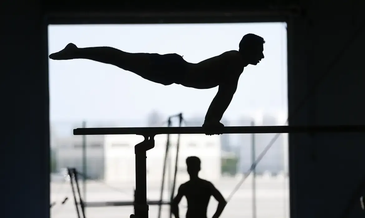 Atleta realizando exercício de ginástica com apoio em barras fixas.