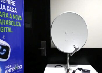 Kit da antena parabólica digital gratuita do programa Siga Antenado, com equipamentos e cartaz informativo ao lado.