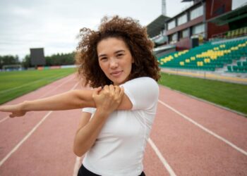 Atleta feminina se alongando no campo de esportes antes de um treino, com foco na preparação física para competições