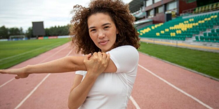 Atleta feminina se alongando no campo de esportes antes de um treino, com foco na preparação física para competições