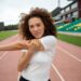 Atleta feminina se alongando no campo de esportes antes de um treino, com foco na preparação física para competições