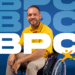 Pessoa sorrindo em uma cadeira de rodas, com o destaque para o logo do BPC (Benefício de Prestação Continuada) e elementos gráficos coloridos ao fundo.