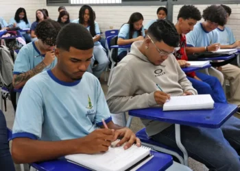 Estudantes em sala de aula, concentrados enquanto escrevem em seus cadernos.
