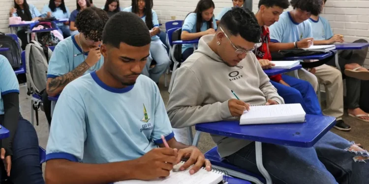 Estudantes em sala de aula, concentrados enquanto escrevem em seus cadernos.