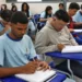Estudantes em sala de aula, concentrados enquanto escrevem em seus cadernos.