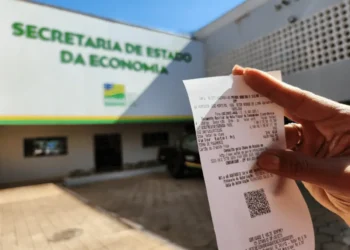 Pessoa segurando uma nota fiscal perto do prédio da Secretaria da Economia.