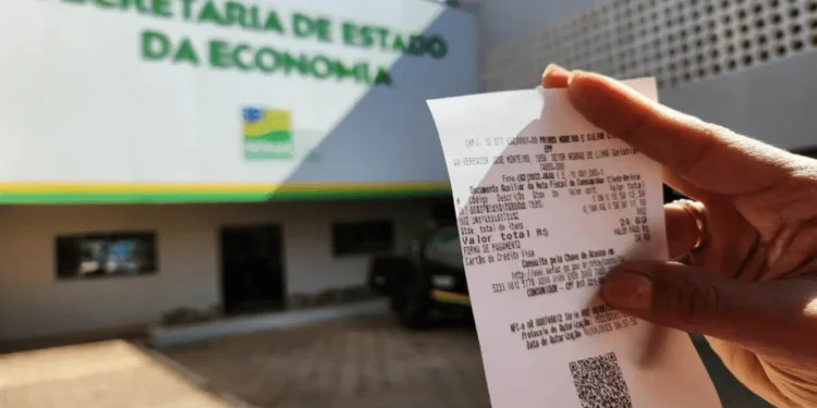 Pessoa segurando uma nota fiscal perto do prédio da Secretaria da Economia.