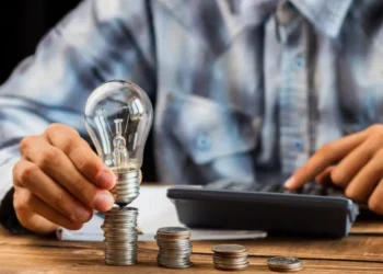 Pessoa calculando valores com moedas e lâmpada, representando a economia na conta de luz com a Tarifa Social.