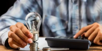 Pessoa calculando valores com moedas e lâmpada, representando a economia na conta de luz com a Tarifa Social.