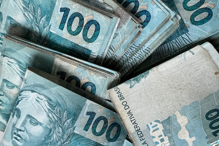 Notas de 100 reais organizadas em maços, representando pagamentos retroativos do INSS.