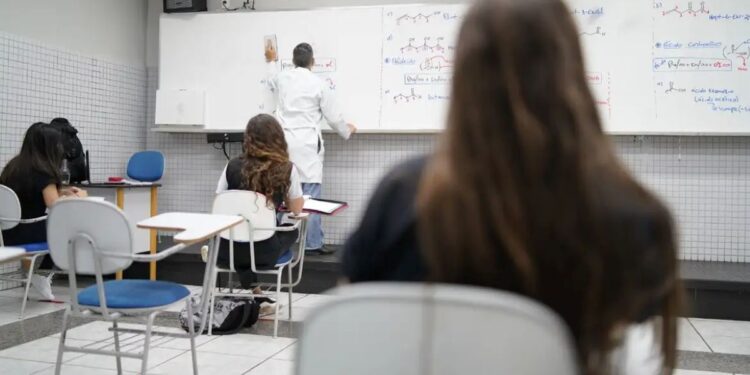 Alunos em sala de aula acompanhando a explicação do professor em quadro branco.