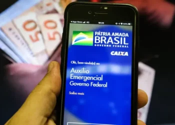 Tela do aplicativo da Caixa Econômica Federal, exibindo informações sobre o Auxílio Emergencial, com cédulas de dinheiro ao fundo.