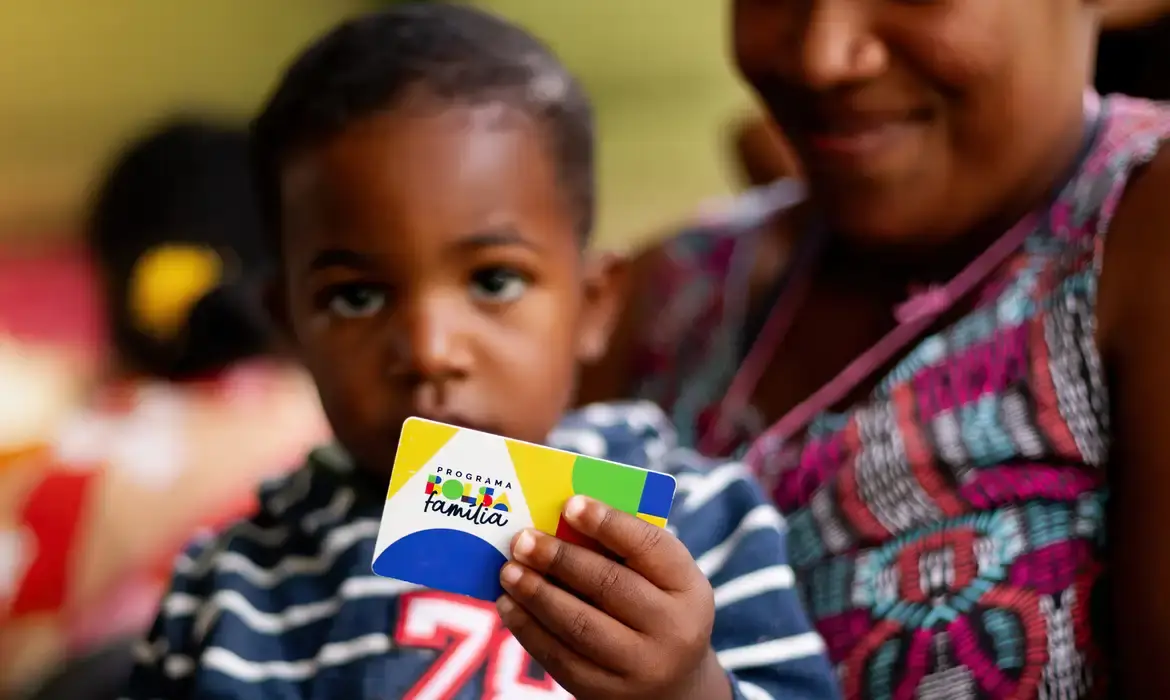 Criança segurando o cartão do Programa Bolsa Família, ilustrando o Benefício Variável Familiar.