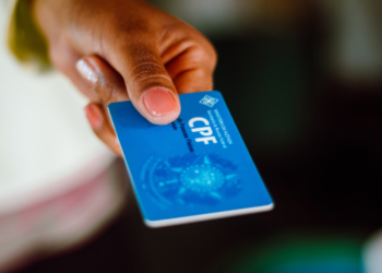 Cartão de CPF sendo segurado por uma mão, com foco no risco de golpes financeiros envolvendo esse documento.