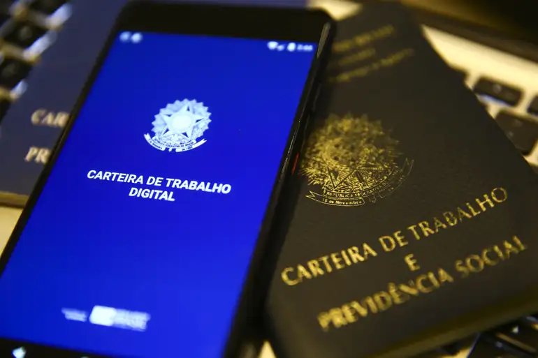 Celular exibindo a Carteira de Trabalho Digital ao lado de documentos financeiros.