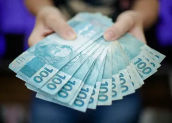 Notas de 100 reais sendo exibidas por uma pessoa.