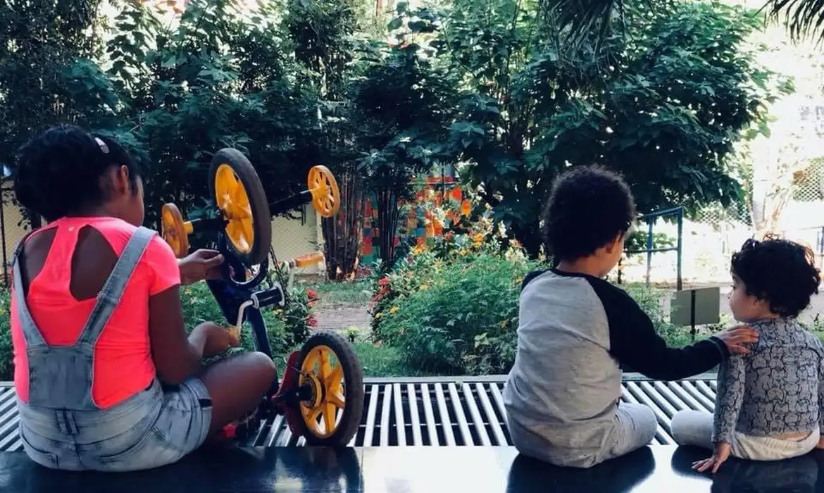 Três crianças brincando em um jardim, simbolizando a faixa etária atendida pelo programa Mães de Pernambuco.